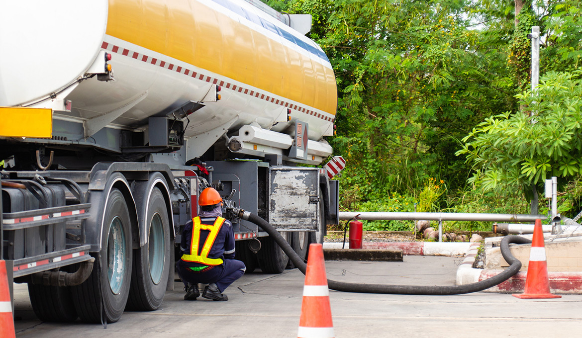 Large truck and maintenance worker delivering fuel to an underground storage tank.