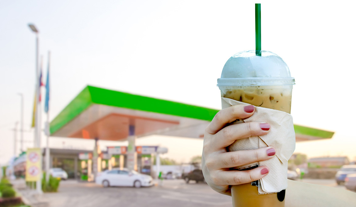 Close up of a hand with an iced coffee drink at the forecourt, fueling up before a summer road trip.