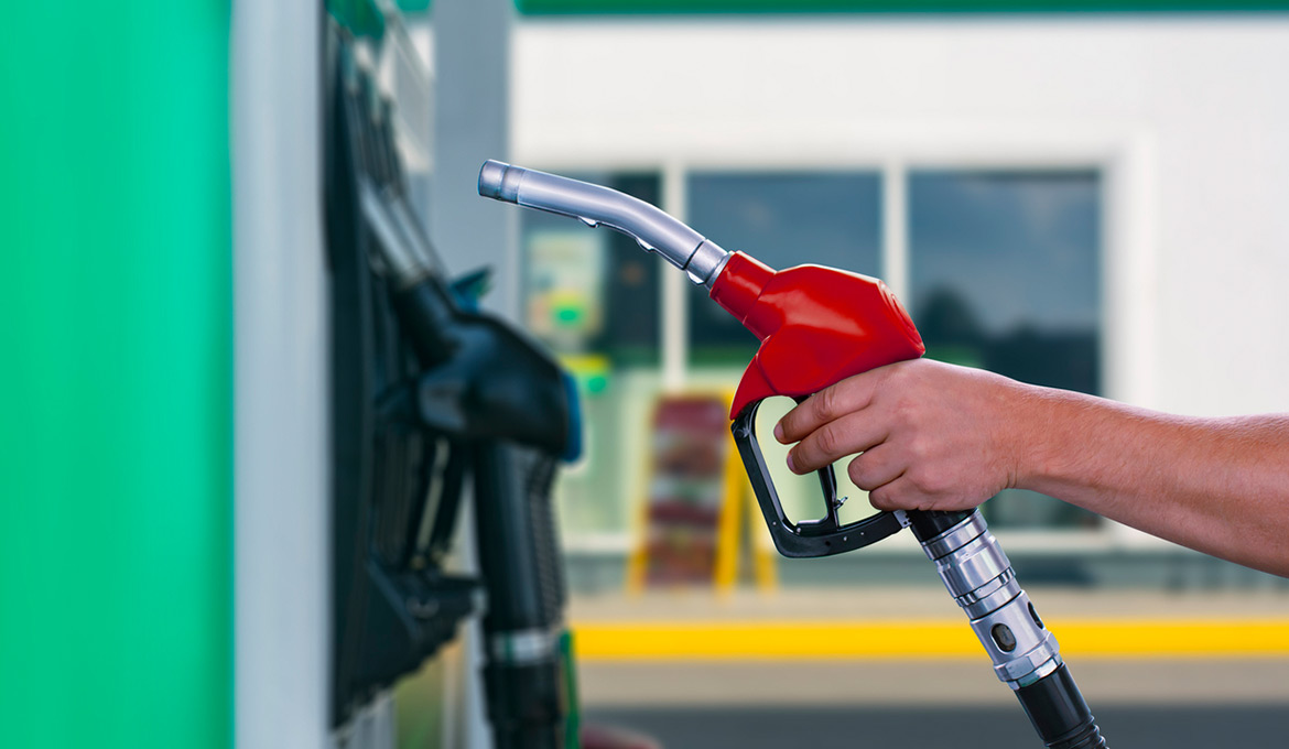Man lifting a fuel nozzle from the dispenser at the forecourt.