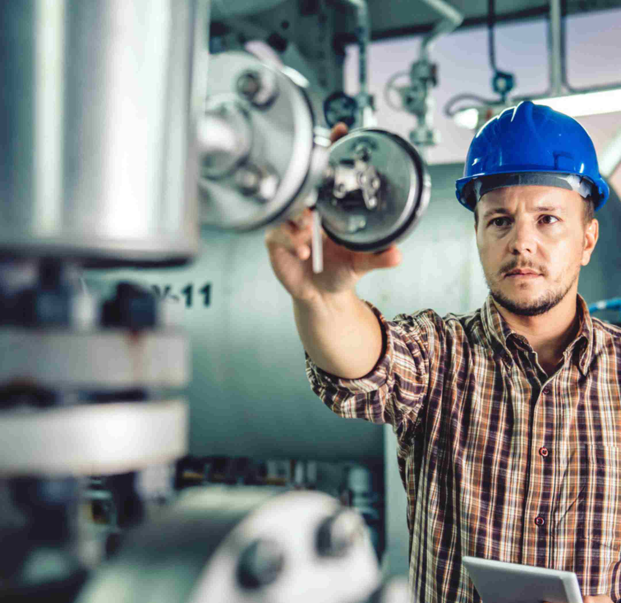 Man in a blue helmet looking at gauges in a facility.