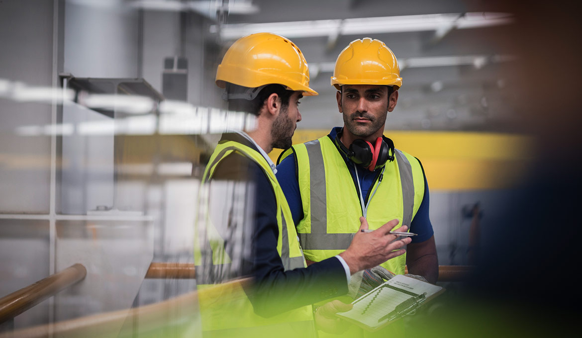 Two male facility workers in safety gear and hard hats conducting an inspection.