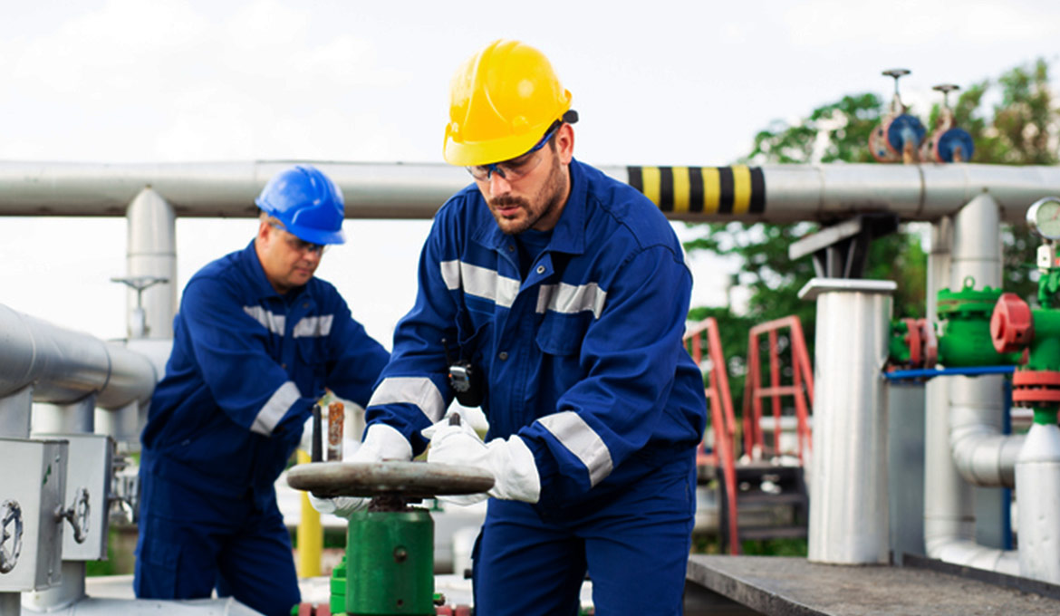 Two facility workers in uniform, safety gear and hard hats working in the field.