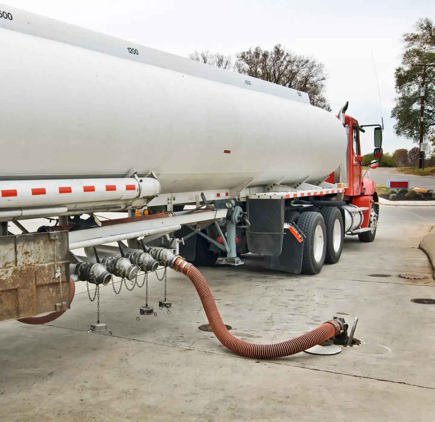 Large fuel truck delivering fuel to an underground tank at a convenience store.