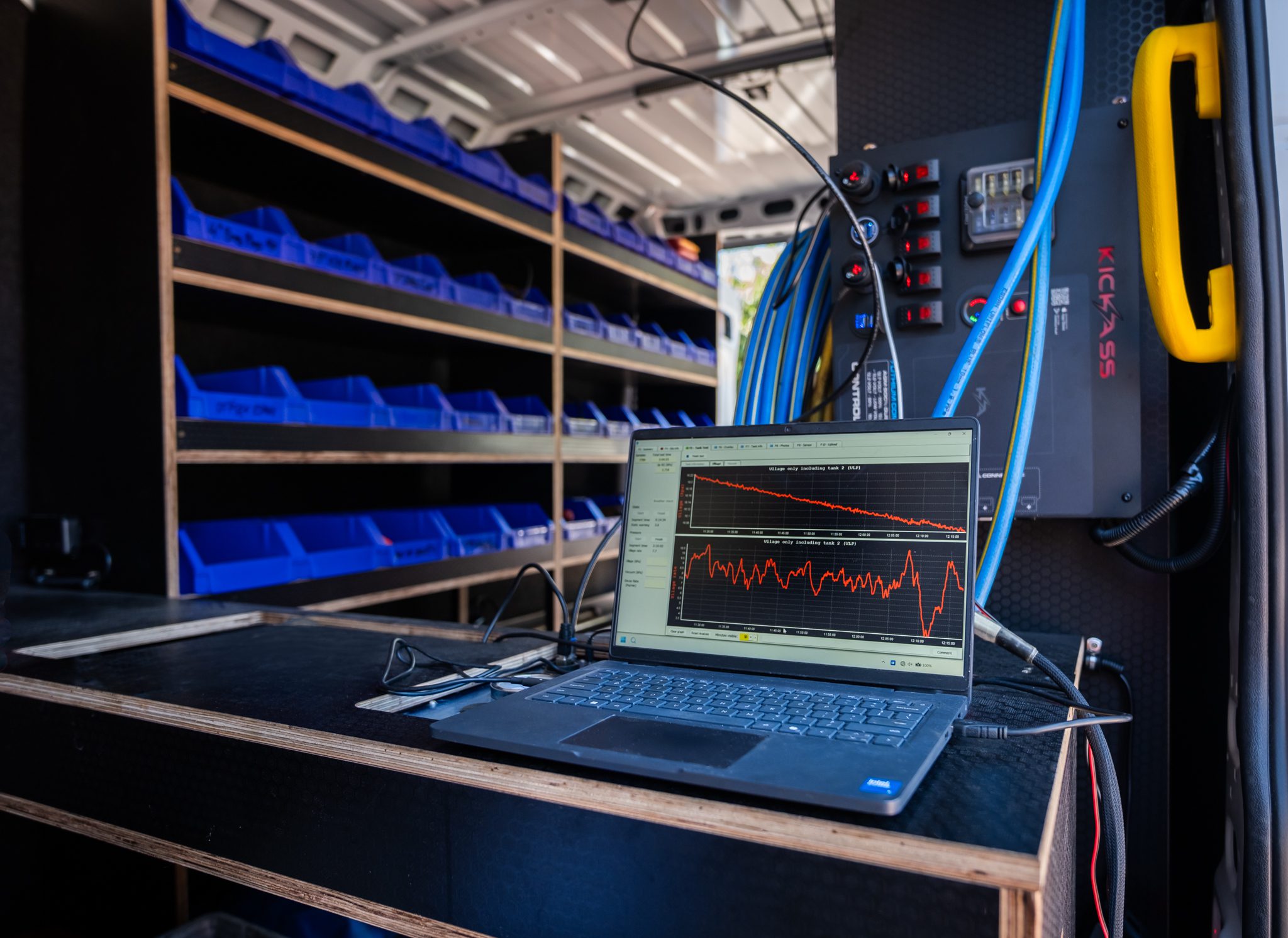 Laptop displaying quantitative tank testing data beside diagnostic equipment inside a service van